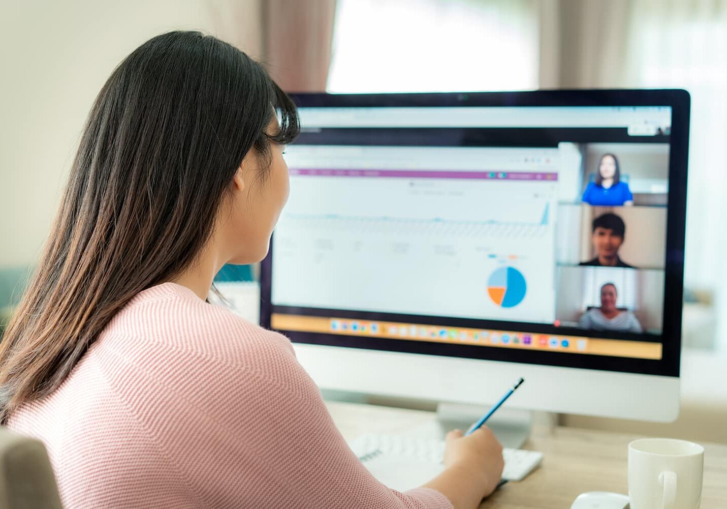 Back view of Asian business woman talking to her colleagues about plan in video conference. Multiethnic business team using computer for a online meeting in video call. Group of people smart working from home.